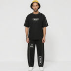 MONROE STORE unisex black cotton blend heavyweight barrel leg sweatpants with white piping and graphic print details.