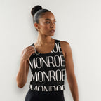 Mujer con camiseta de tirantes negra MONROE STORE con estampado gráfico, en un estudio de danza con espejo.