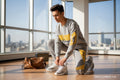 MONROE STORE grey cotton tracksuit with yellow accents, worn by a man tying his white sneakers in a bright studio.